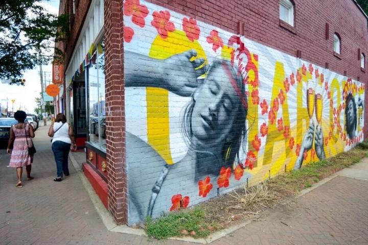 A mural painted on red brick. The mural is a picture of a relaxed woman brushing her hair back with her hand and two Stella Artois glasses clinking.